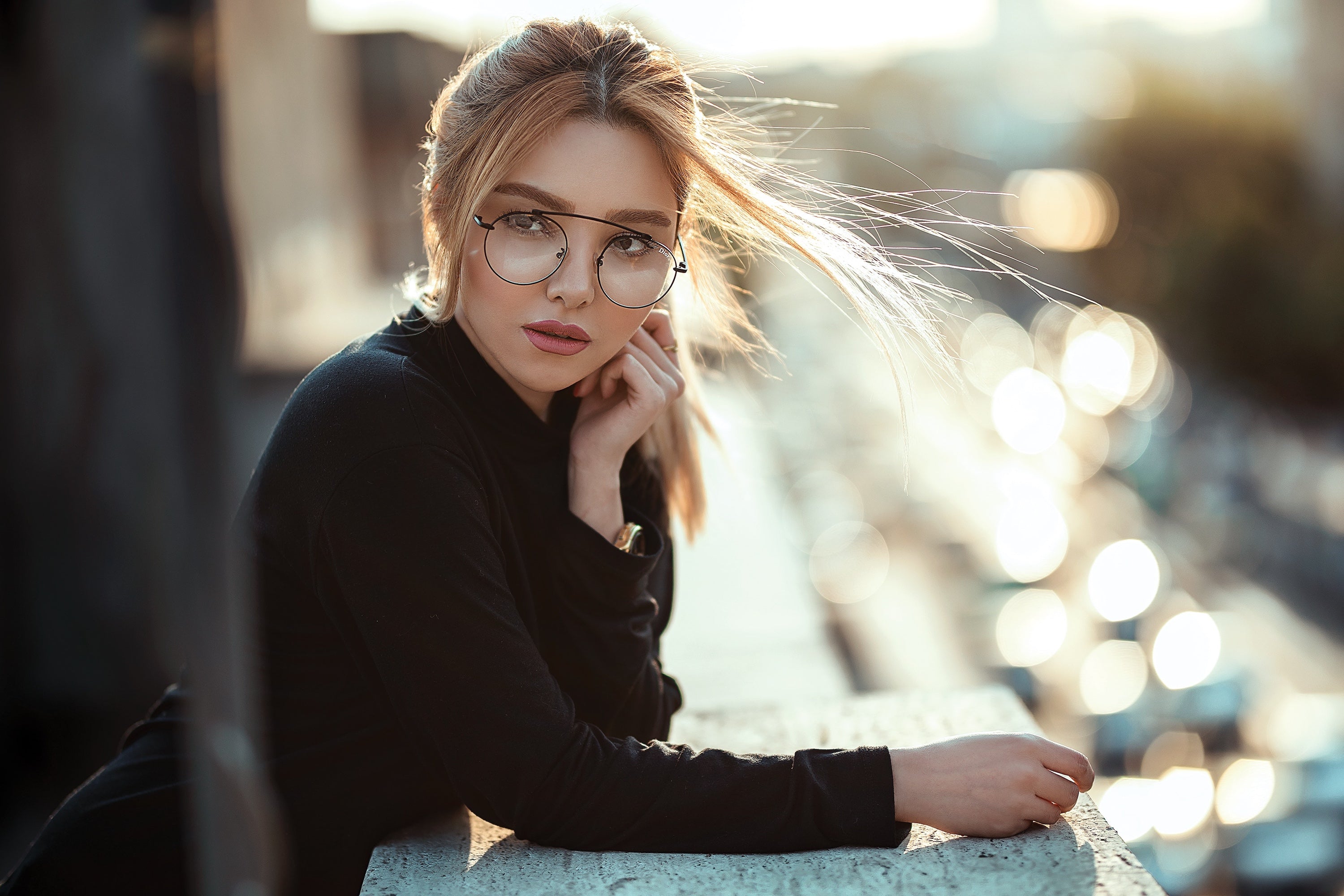 Woman wearing glasses and a black jacket with blurred lights in the background