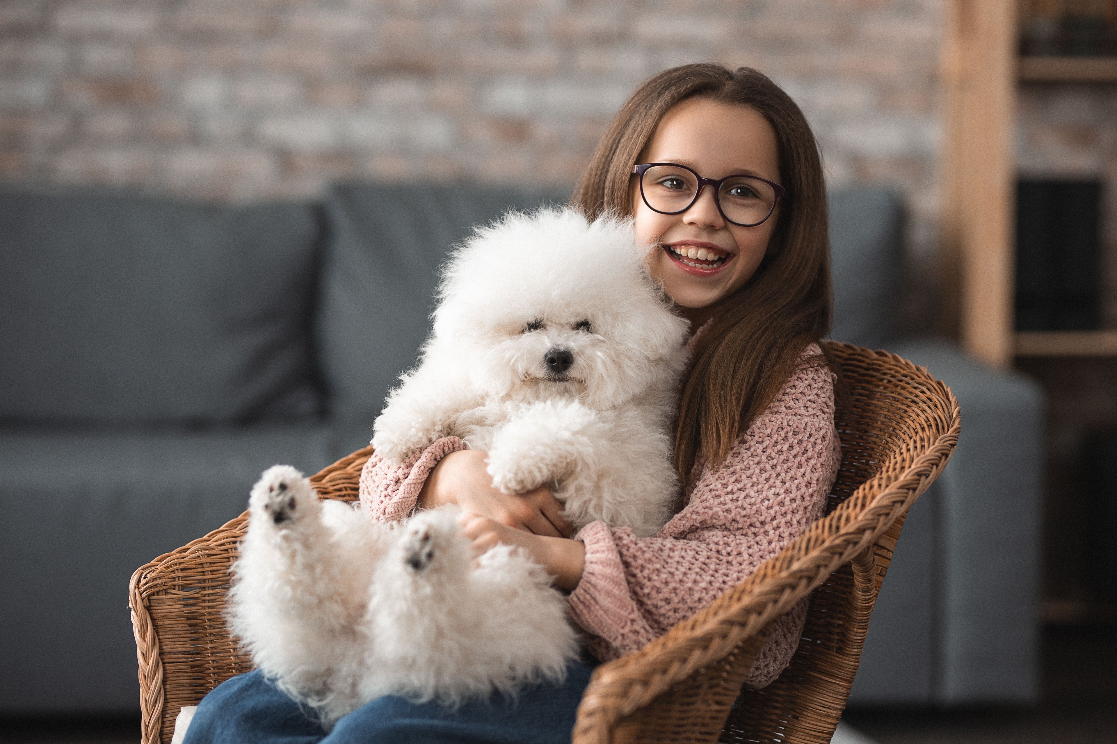 Girl holding a small white dog in a wicker chair