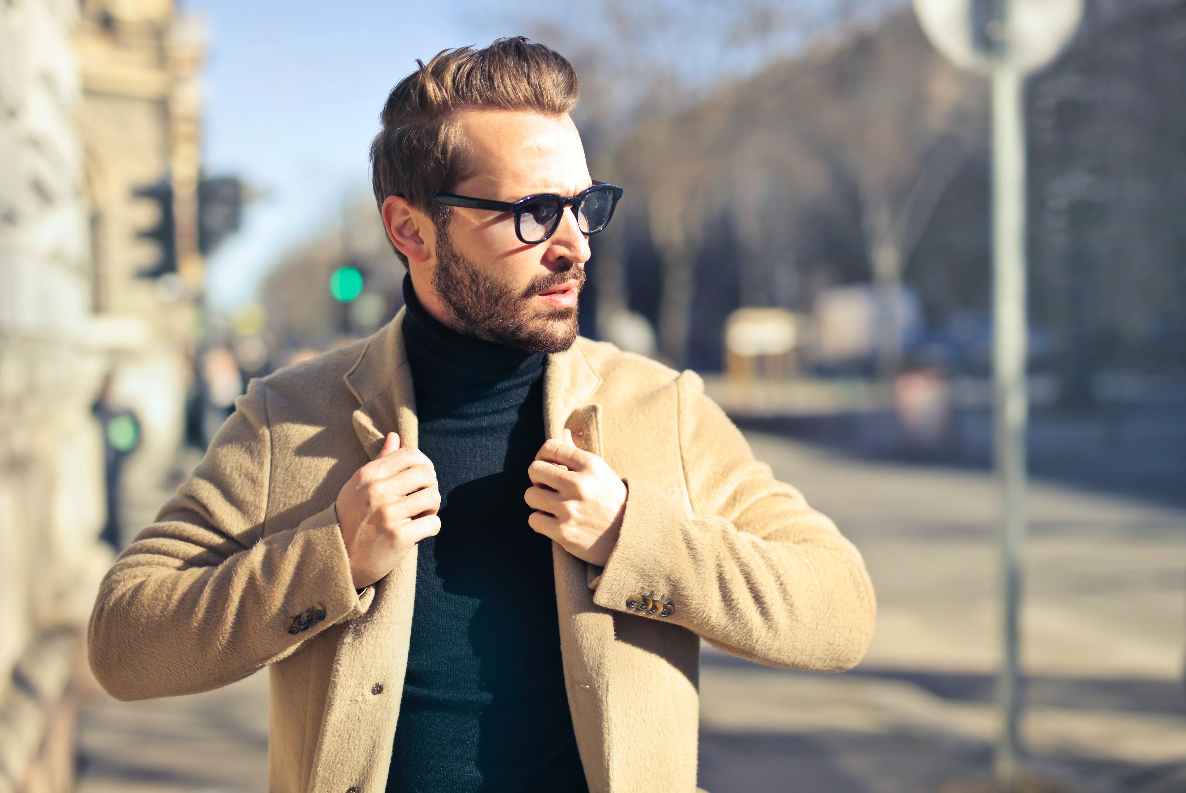 Man wearing a beige coat and sunglasses on a city street